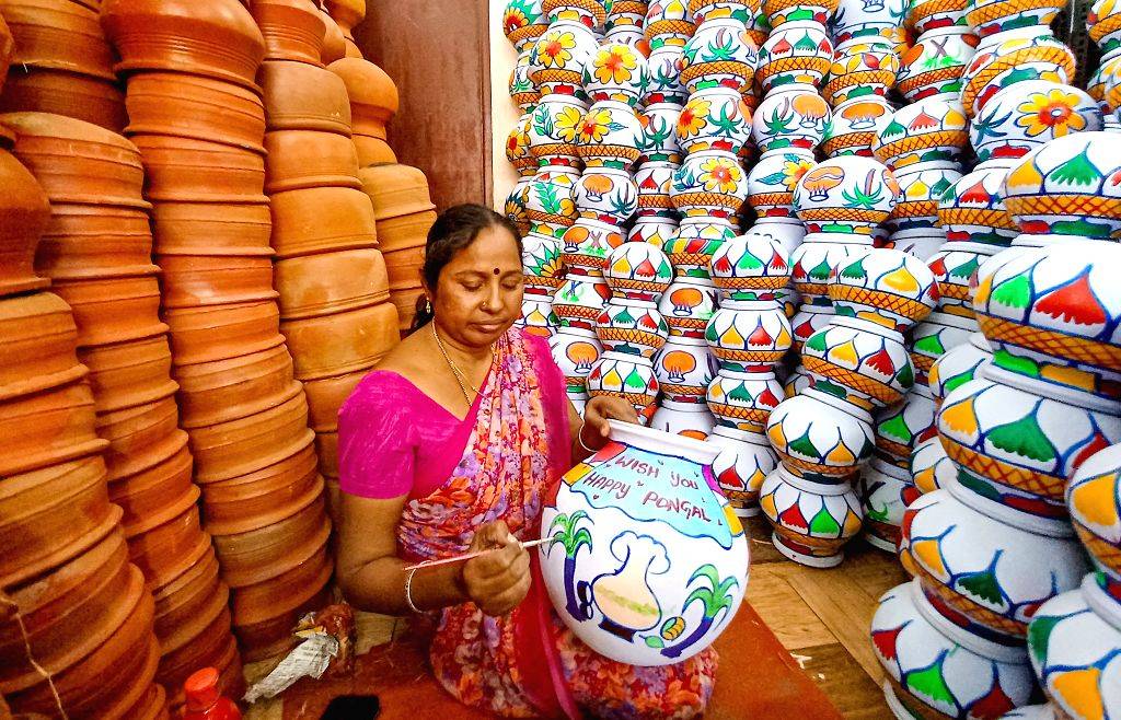 A woman decorates earthenware pots with vibrant designs