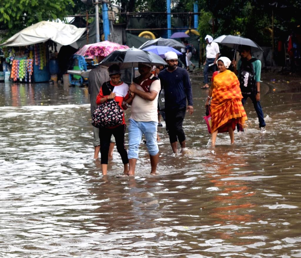 Commuters wade through a waterlogged road after heavy rain