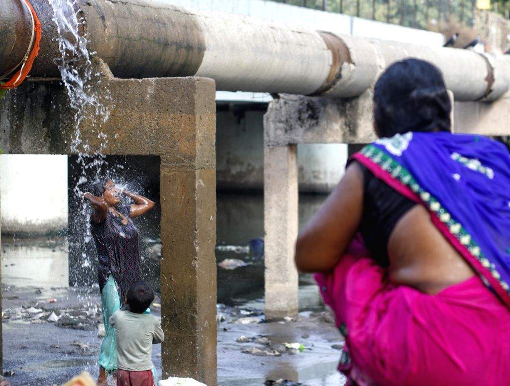 People take a bath at a broken water pipeline during a hot summer afternoon
