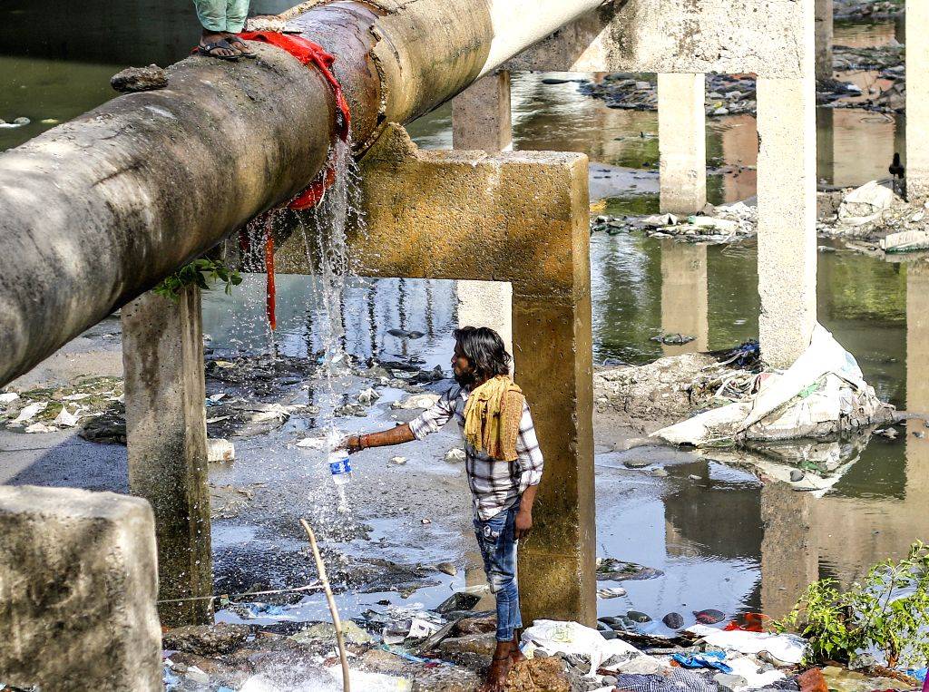 People take a bath at a broken water pipeline during a hot summer afternoon