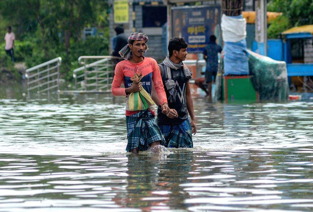 People wade through a flooded road after heavy rainfall owing to ...